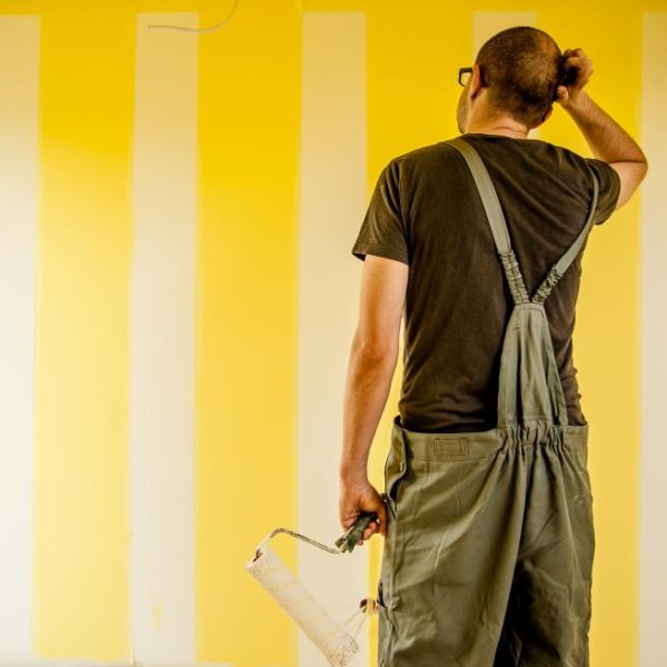 curious homeowner in overalls staring at wall with painted yellow stripes