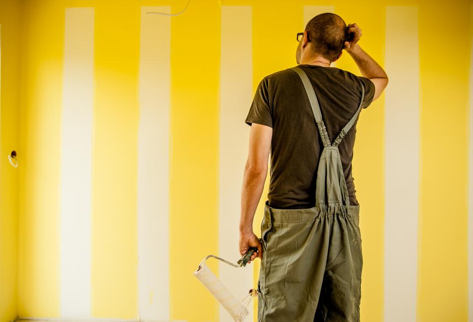 curious homeowner in overalls staring at wall with painted yellow stripes