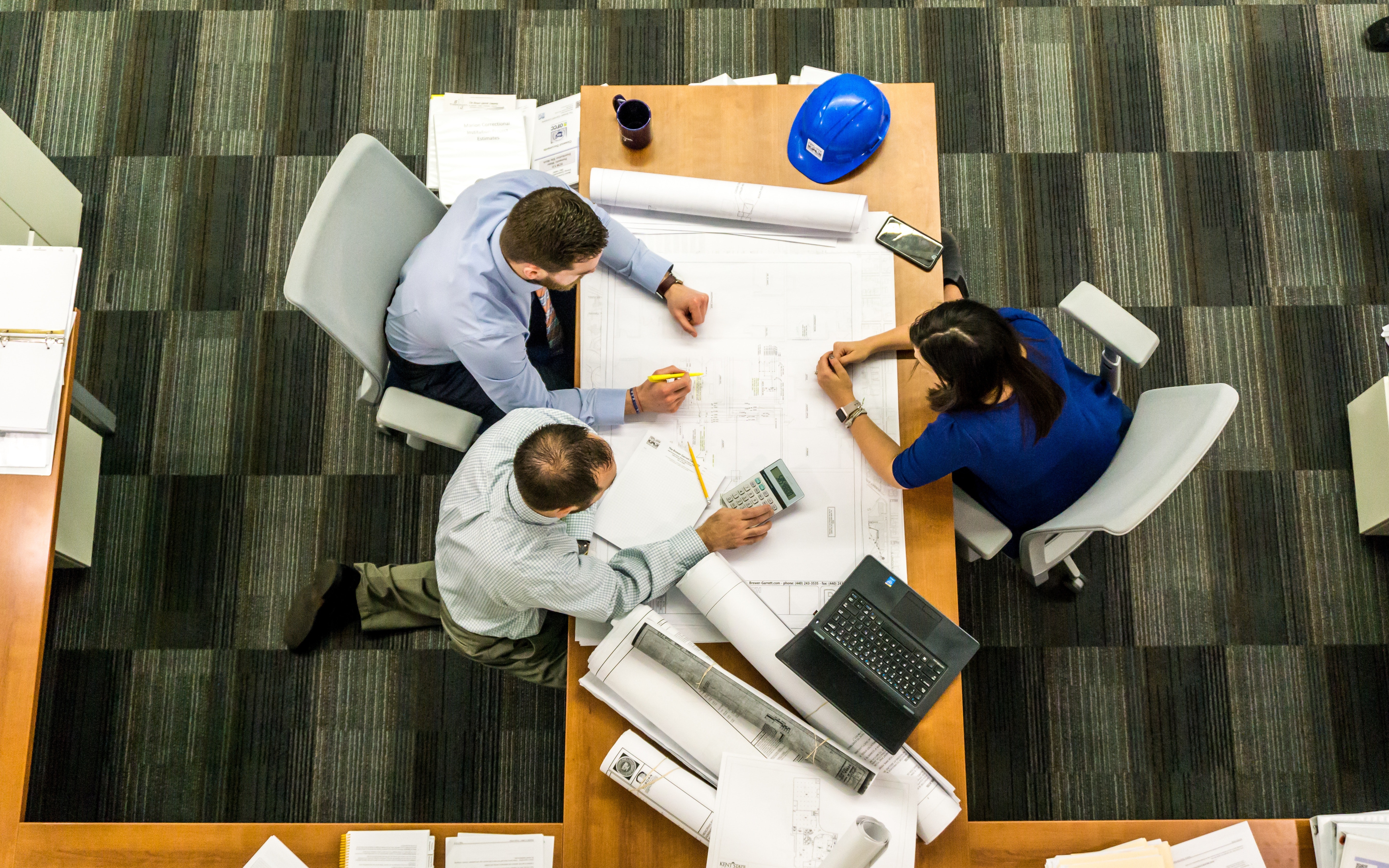 Birds eye view of three people reviewing plans for commercial property renovation