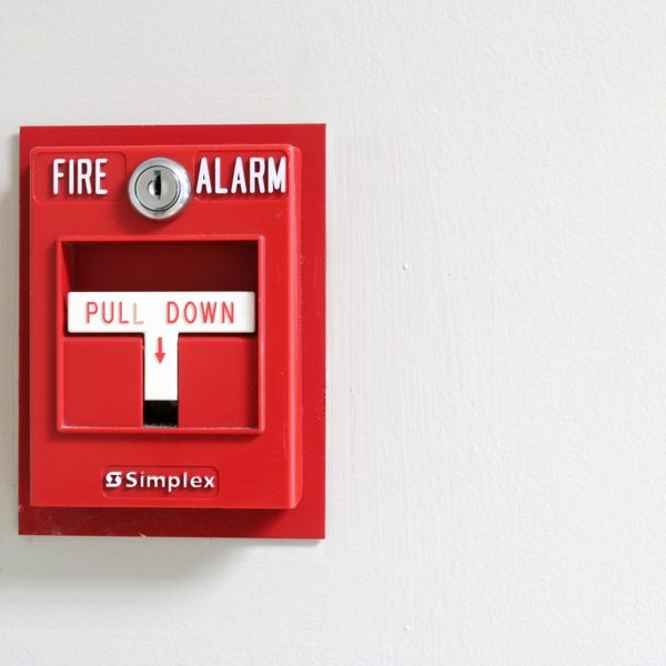 Close up view of red commercial fire alarm against white wall