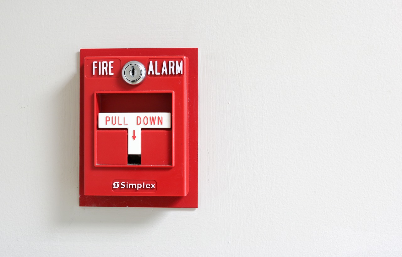 Close up view of red commercial fire alarm against white wall