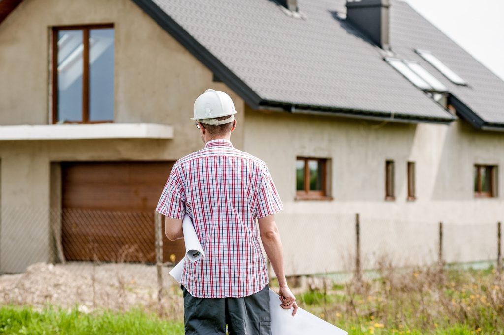 Contractor approaching adobe home with renovation plans in hand