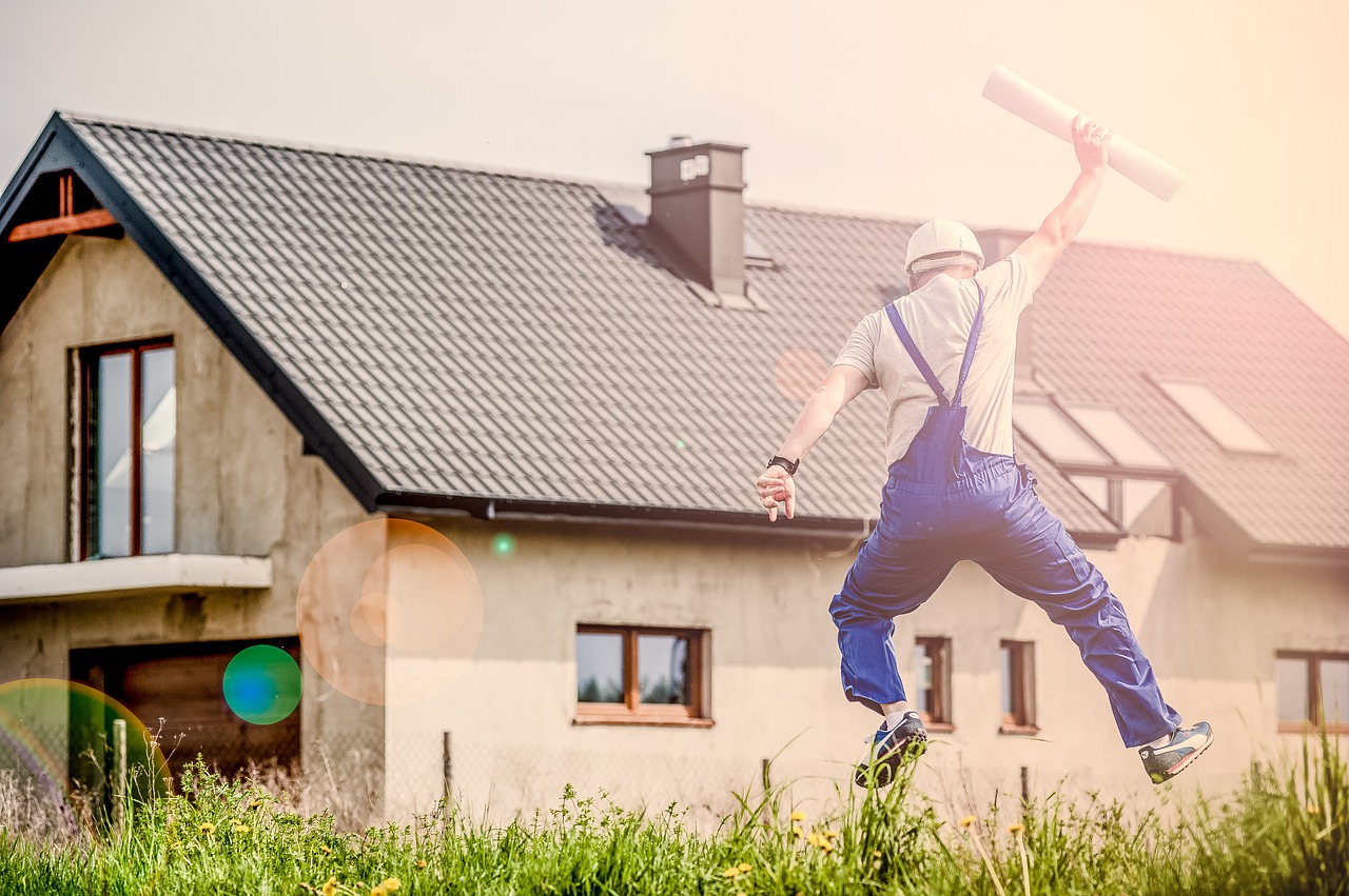 Man in blue contractor's overalls jumping for joy and holding plans in air