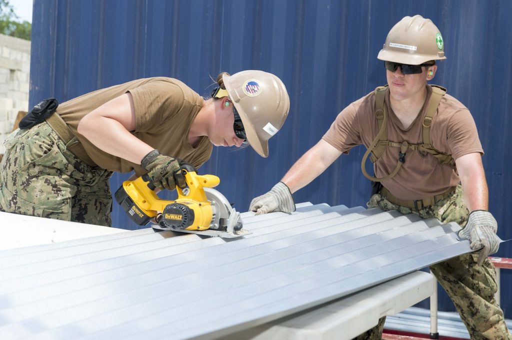 Two military contractors cutting corrugated steel sheet