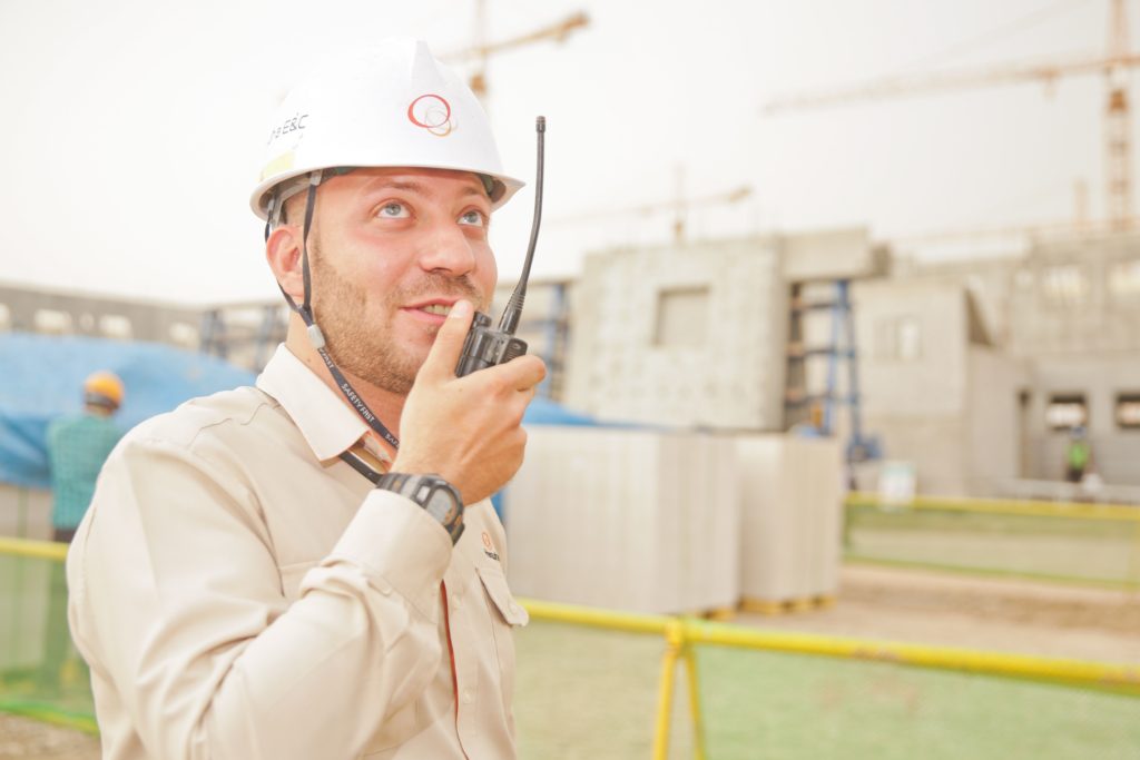 Worker in beige shirt and white hard hat talking on walkie talkie