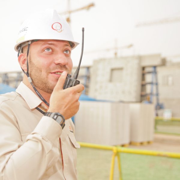 Worker in beige shirt and white hard hat talking on walkie talkie