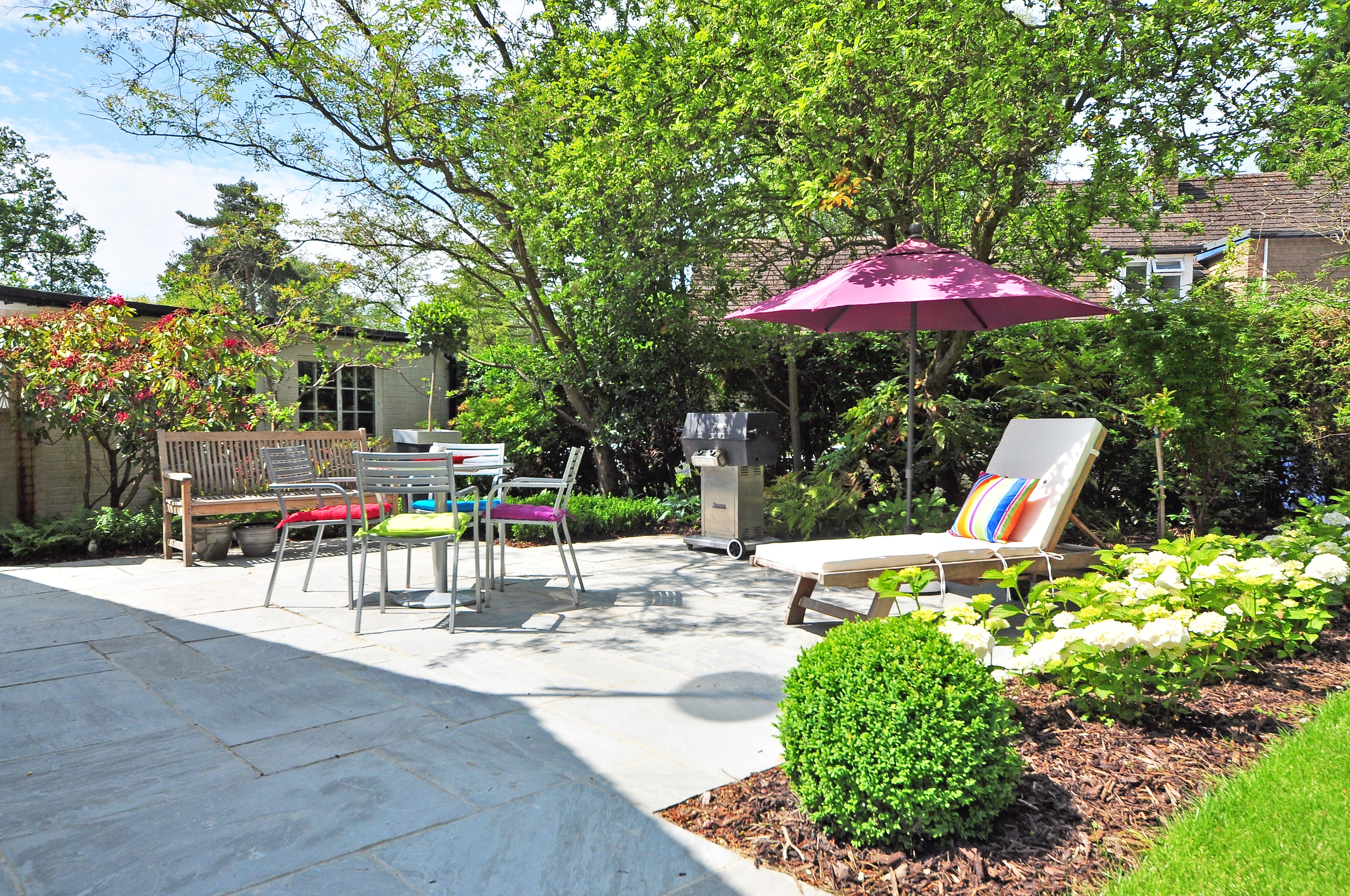 paved backyard patio with seating area, umbrella, and lounge chair