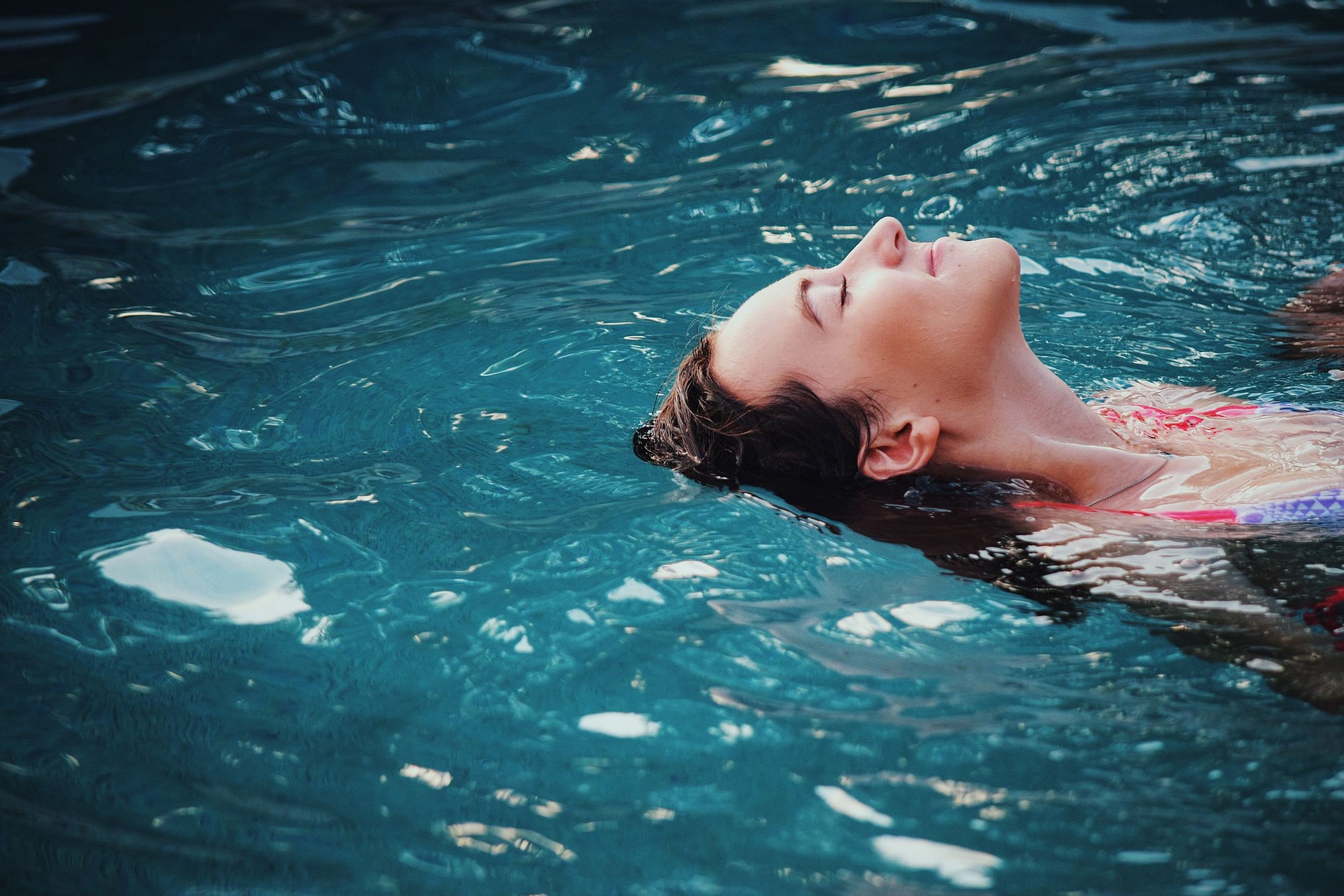 woman with eyes closed, leaning back and relaxing in a pool