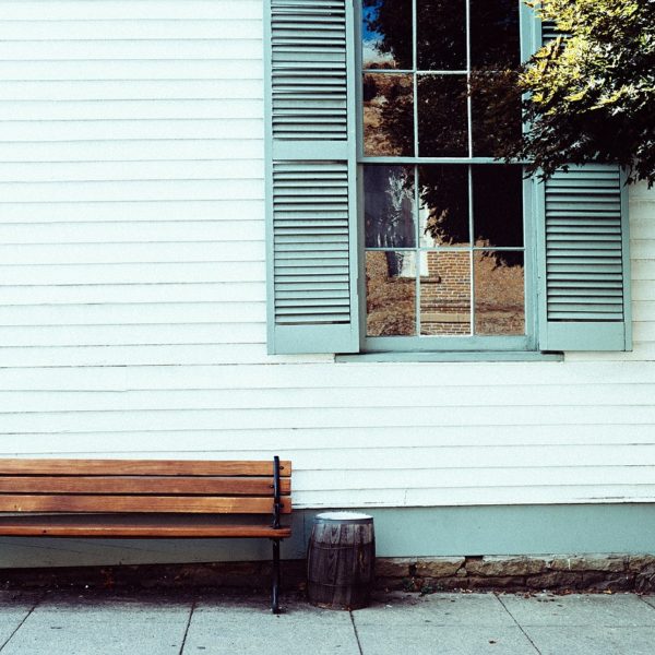 old white siding on home, view of window with green shutters and wooden bench outside house