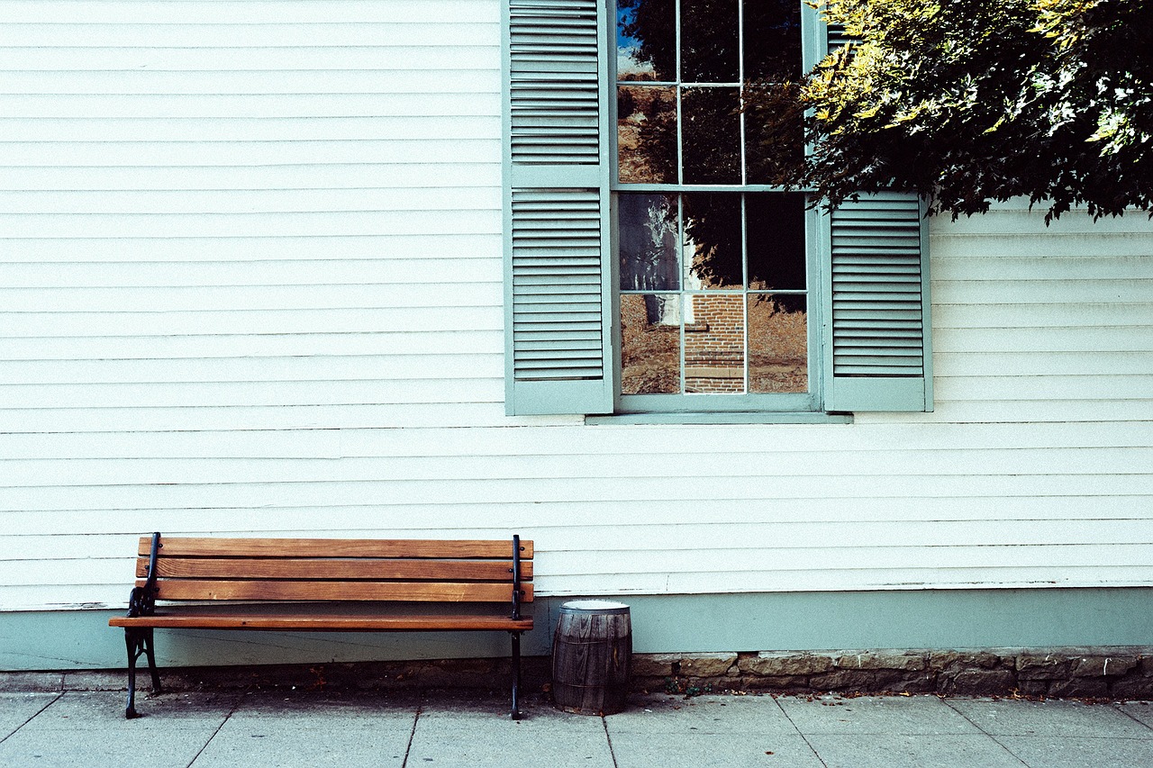 old white siding on home, view of window with green shutters and wooden bench outside house