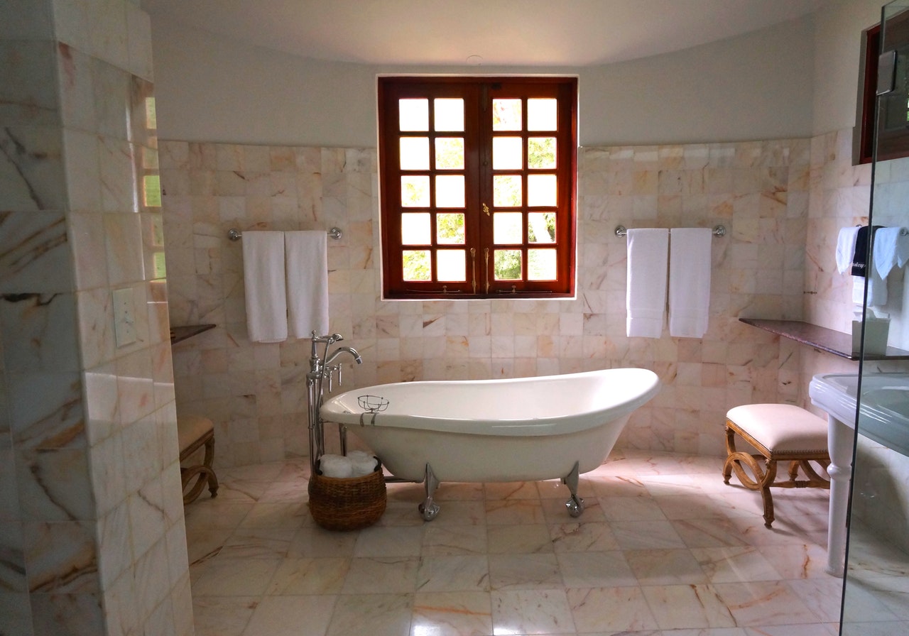 renovated home bathroom with marble tile on walls and beautiful clawfoot tub in center of room