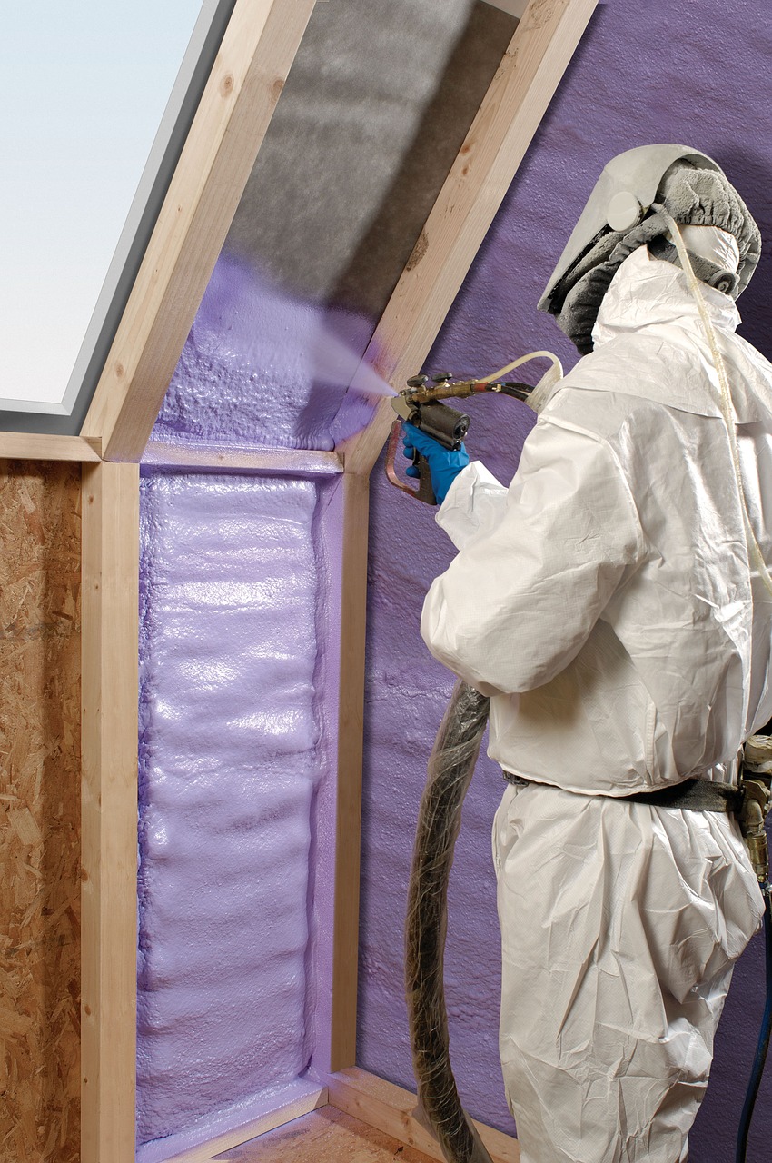 A man in a white body suit spraying purple insulation