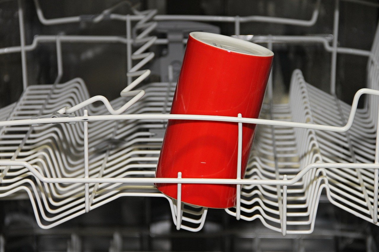 a dishwasher with white wire trays and a single red cylindrical cup