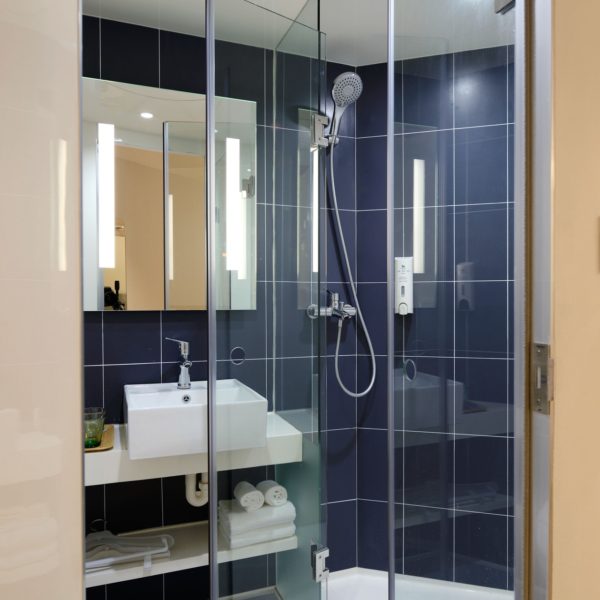 stand up shower with blue tiles and glass doorway