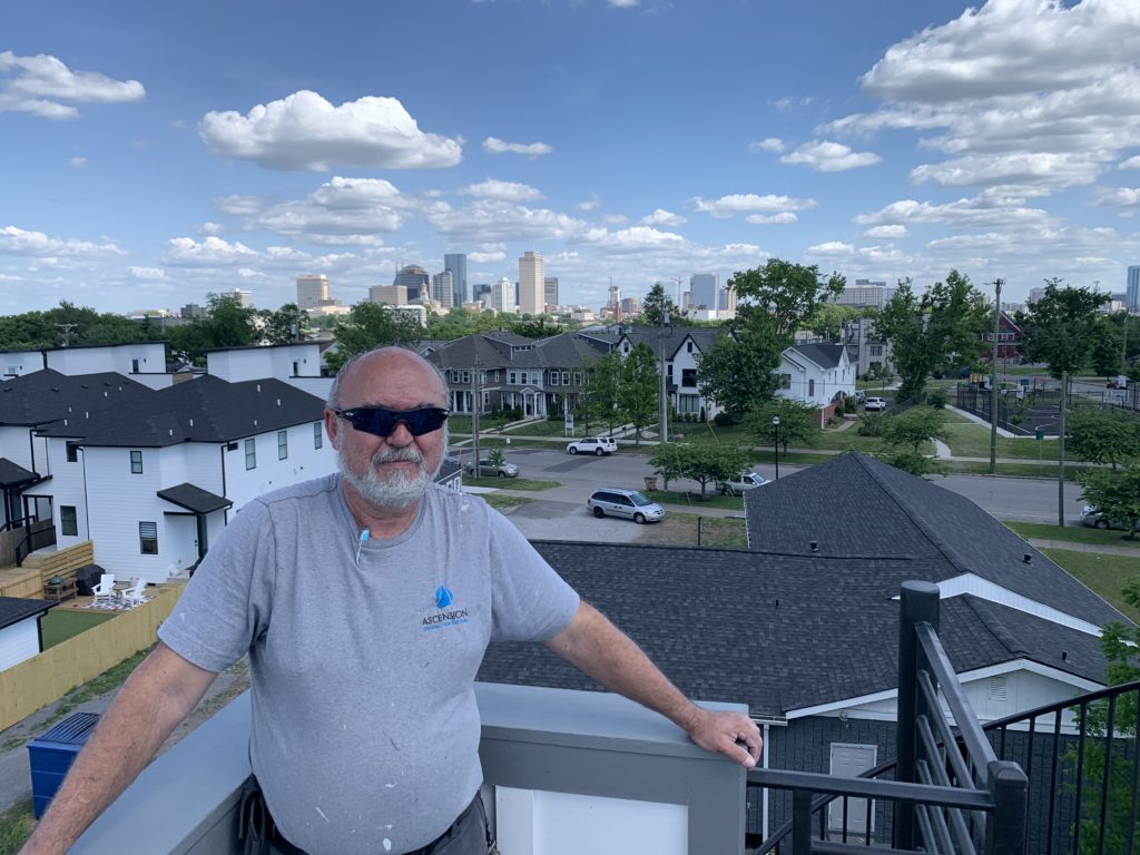 Man standing on balcony with Nashville skyline in the background, blue skies and cloudy