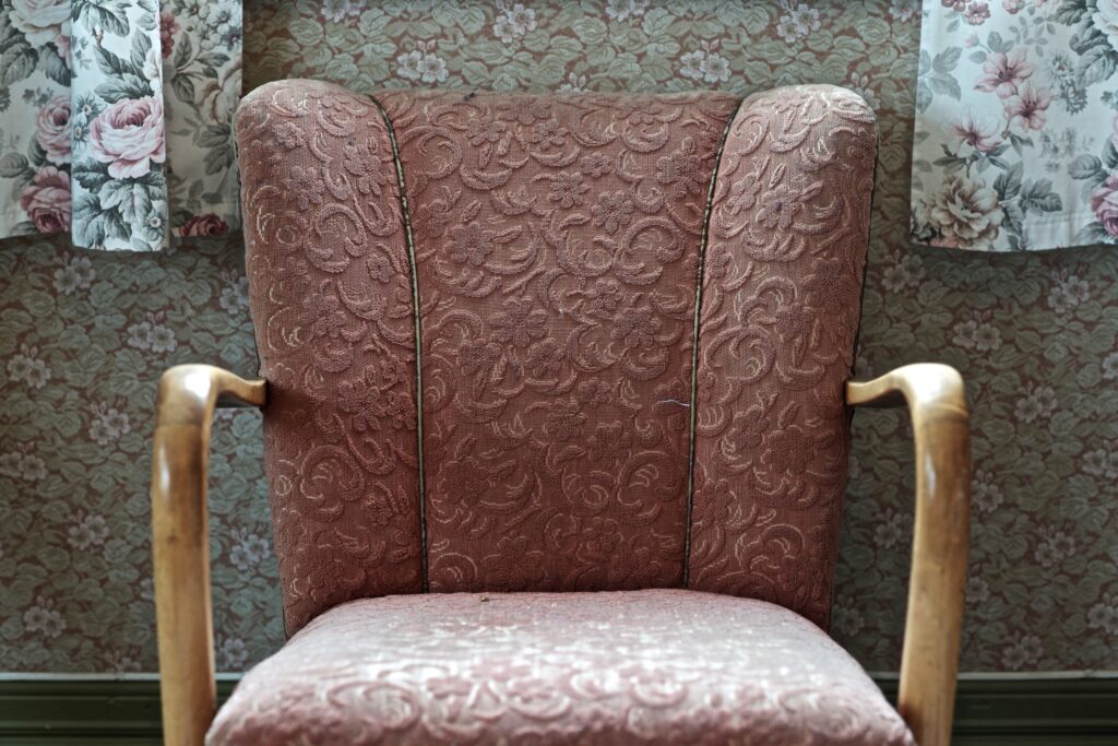 A weathered vintage chair in front of a wallpapered wall.