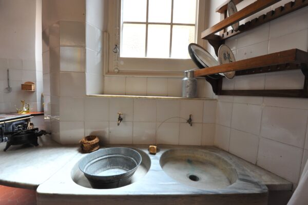 Rustic sink with metal bucket in a white-tiled kitchen.